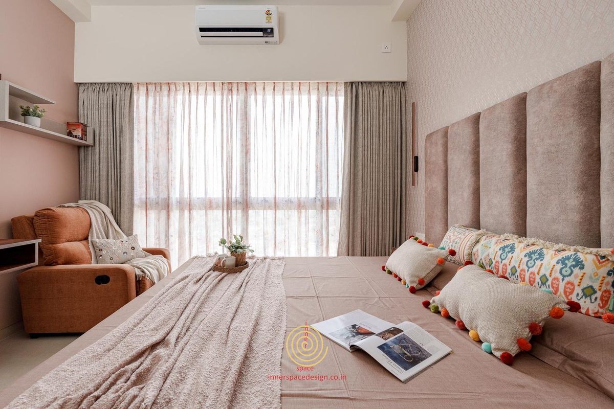 Blush bedroom with a reading chair beside the window and a wide upholstered headboard