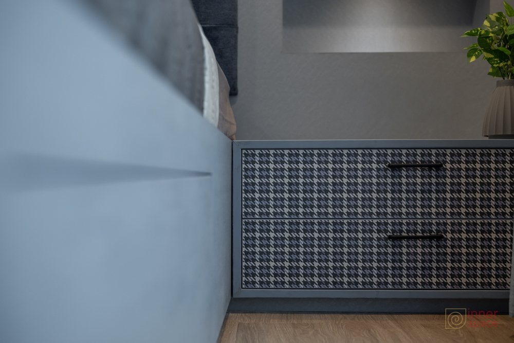 Bedside drawer unit with a houndstooth patterned front beside an upholstered bed